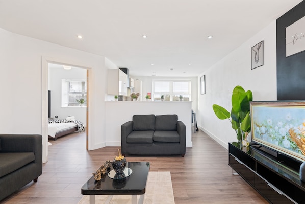 A modern living room with a grey sofa, a coffee table with decorative items, a flat-screen TV, and a large plant.