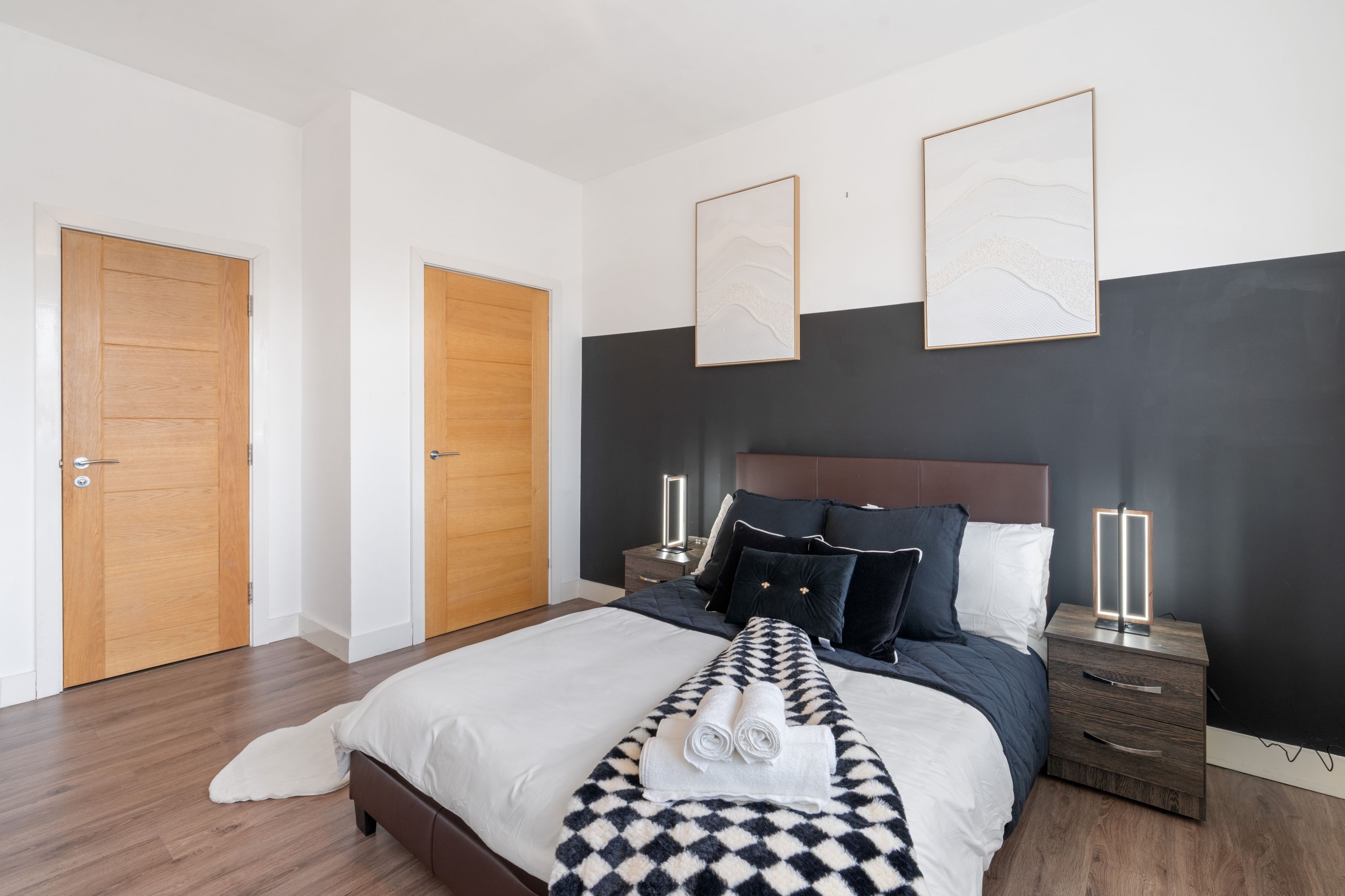 A modern bedroom with a large bed, wooden doors, and artwork on the walls.