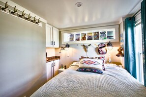 A bedroom with a bed, a nightstand, a wall-mounted shelf with pictures, and a window with curtains. - The Bluebonnet Bungalow with Resort Access (Austin)