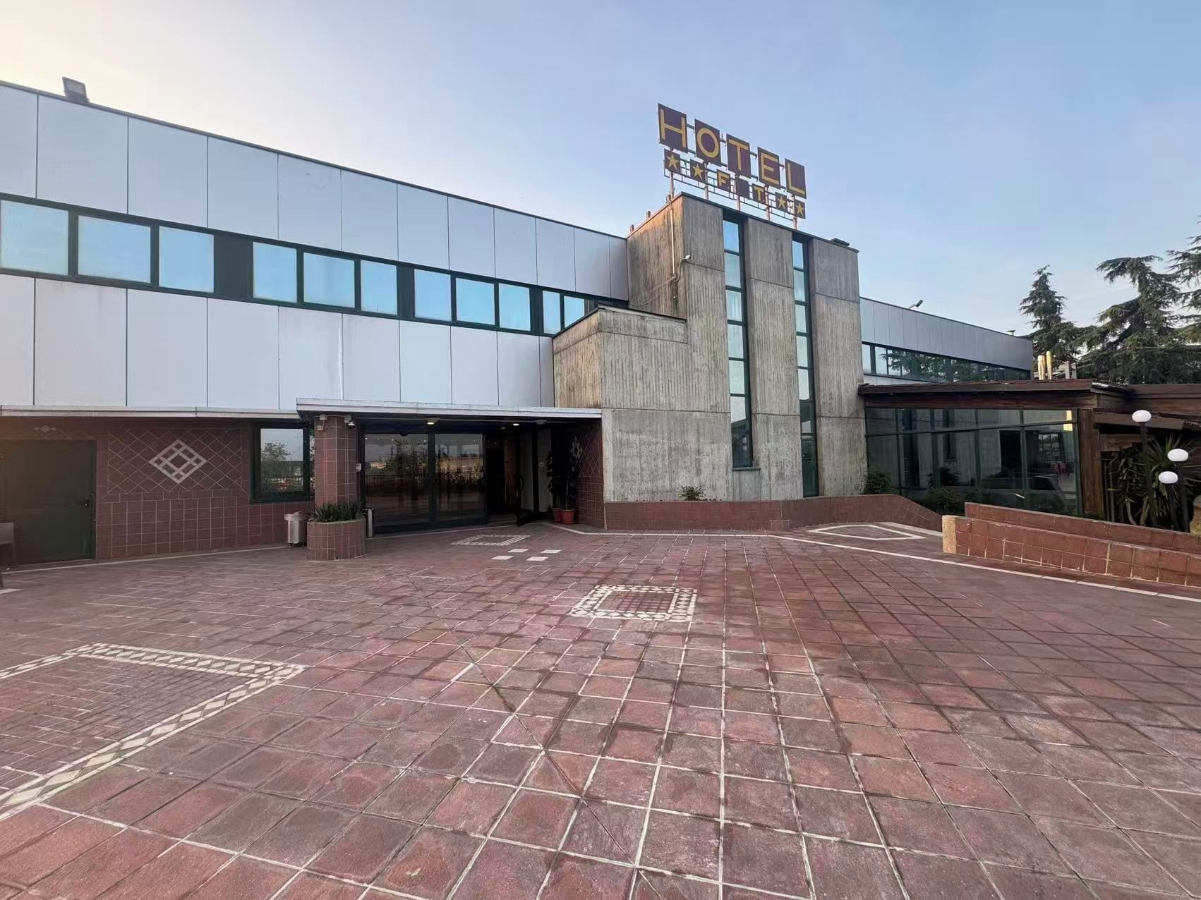 A hotel with a modern exterior, a prominent sign, and a paved courtyard.