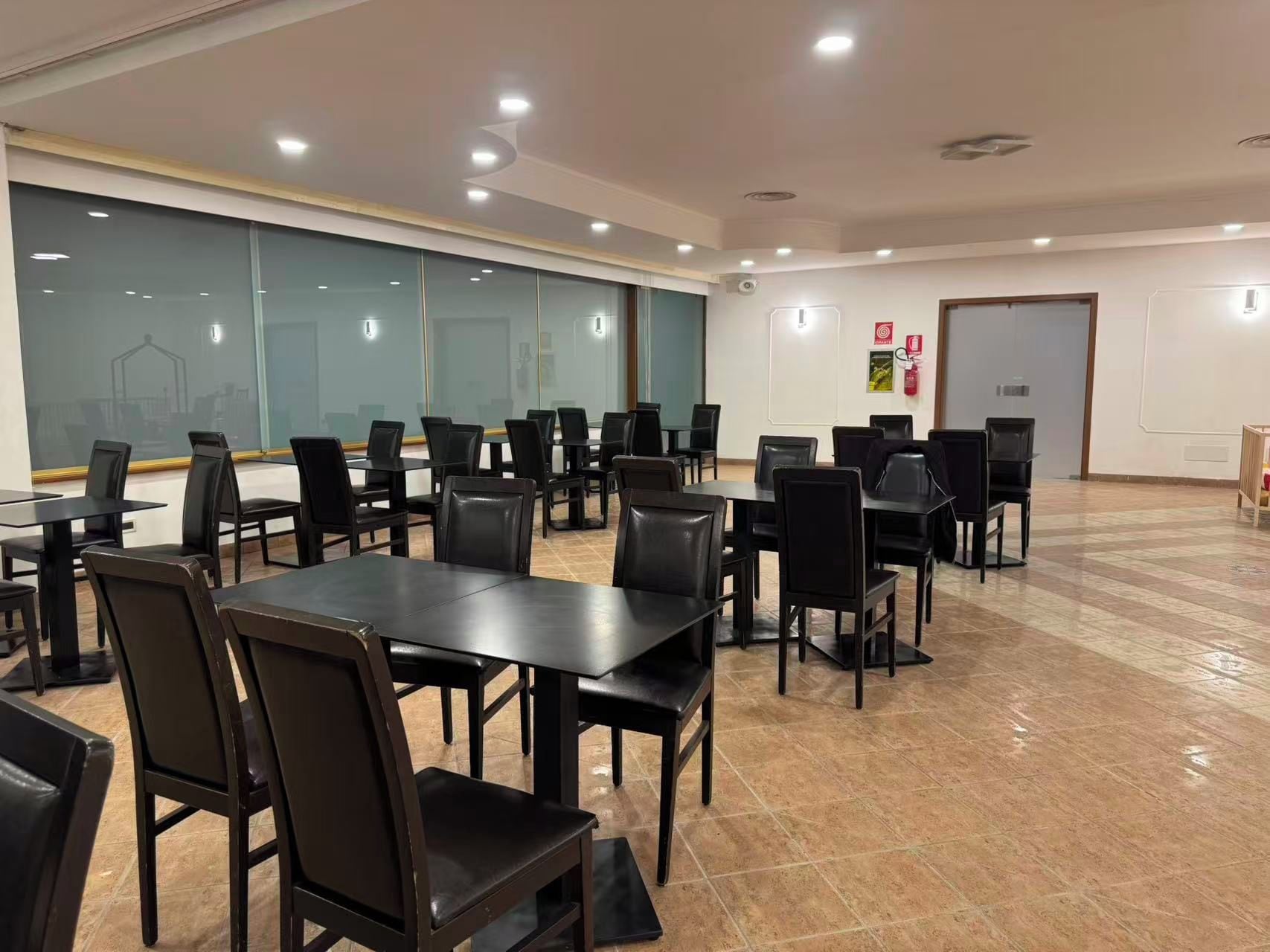 Une salle de conférence équipée de tables et de chaises, de grandes fenêtres et d’une porte.