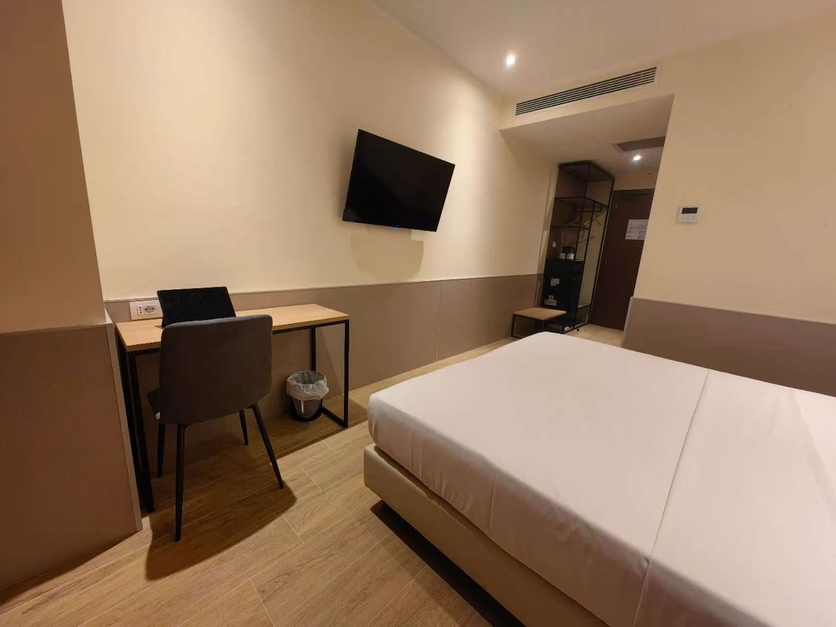 A hotel room with a bed, a desk, a chair, a television, and a wardrobe.