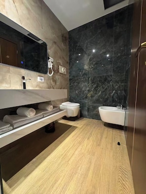 Un baño moderno con pared de mármol, tocador de madera, inodoro, bidé y lavamanos.