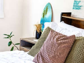 Un dormitorio con cama, almohadas, una tabla de surf y una planta.