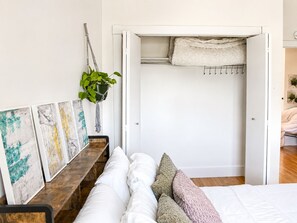 A bedroom with a bed, a bedside table, a hanging plant, and a closet with a towel.