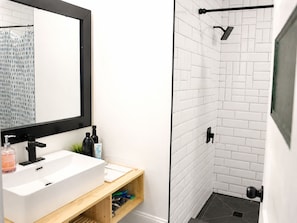 A modern bathroom with a white sink, black faucet, and a mirror with a black frame. There is a shower area with white tiles and a black showerhead. - Pet-Friendly Farmhouse | Weddings, Special Events, Corporate Retreats + More! (Belleville)