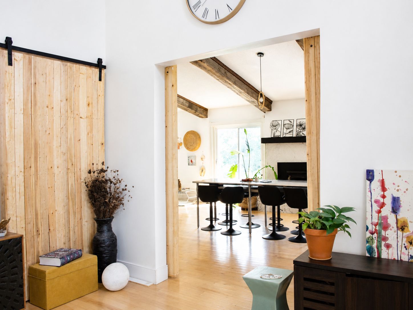 A modern interior with a wooden floor, a black sofa, a dining area with bar stools, and a kitchen in the background.