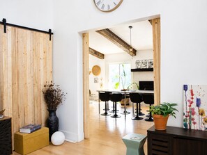 Ein modernes Interieur mit Holzboden, einer schwarzen Couch, einem Essbereich mit Barhocker und einer Küche im Hintergrund.