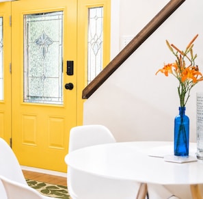 A yellow door with a glass panel, a white chair, a round table, and a blue vase with flowers. - Pet-Friendly Farmhouse | Weddings, Special Events, Corporate Retreats + More! (Belleville)
