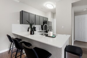 A modern kitchen with a white countertop, dark cabinets, and a stainless steel sink. - Spacious 3-bedroom apartment in Houston (Houston)