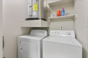 A laundry area with two white washers and dryers, a water heater, and a shelf with cleaning supplies. - Spacious 3-bedroom apartment in Houston (Houston)