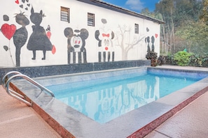 Una piscina amb un mural al mur proper, una escala metàl·lica i un cel blau clar.