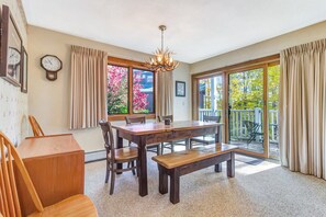 A dining area with a wooden table and chairs, a chandelier, and a view of a balcony with outdoor furniture. - Kettlebrook | True Ski-In/Out | 3BR + Fireplace (Ludlow)