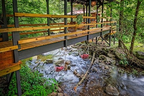 Eine Holzbrücke über einem plätschernden Bach mit Holzboden und Bänken.