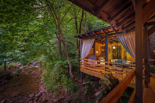 Une cabane en bois dotée d’un balcon donnant sur une zone boisée et un ruisseau.