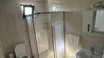 Ein Badezimmer mit Toilette, einer Duschkabine und einem Waschbecken mit Spiegel darüber.