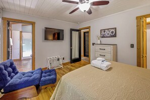 Quarto com cama, área de estar, televisão, cômoda e ventilador de teto.