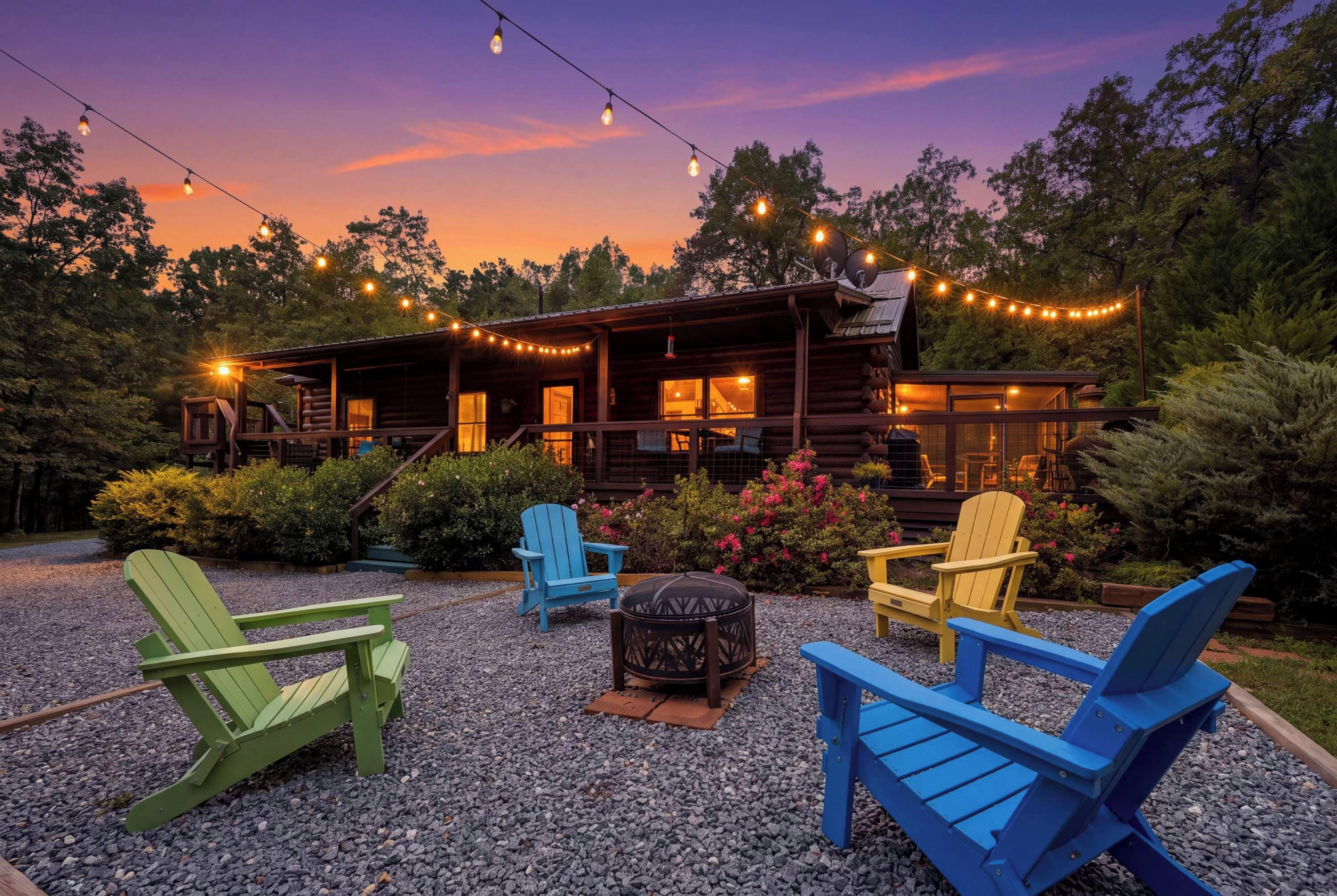 A wooden cabin with a porch, surrounded by gravel, and outdoor seating with Adirondack chairs.
