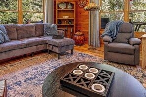Un salon chaleureux avec un canapé d’angle, un fauteuil, une table basse et une bibliothèque agrémentée d’objets décoratifs.