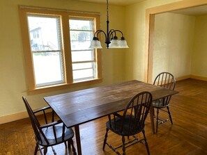 A dining area with a wooden table and four chairs, a hanging light fixture, and a window with a view of buildings outside. - Pet friendly 3-bedroom house in Clarendon next to Allegheny national forest (Clarendon)
