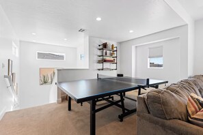 Ein Zimmer mit einem Pingpongtisch, einer Couch und einem Bücherregal mit verschiedenen Gegenständen.