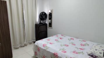 A bedroom with a bed, a dresser, a fan, and a door.