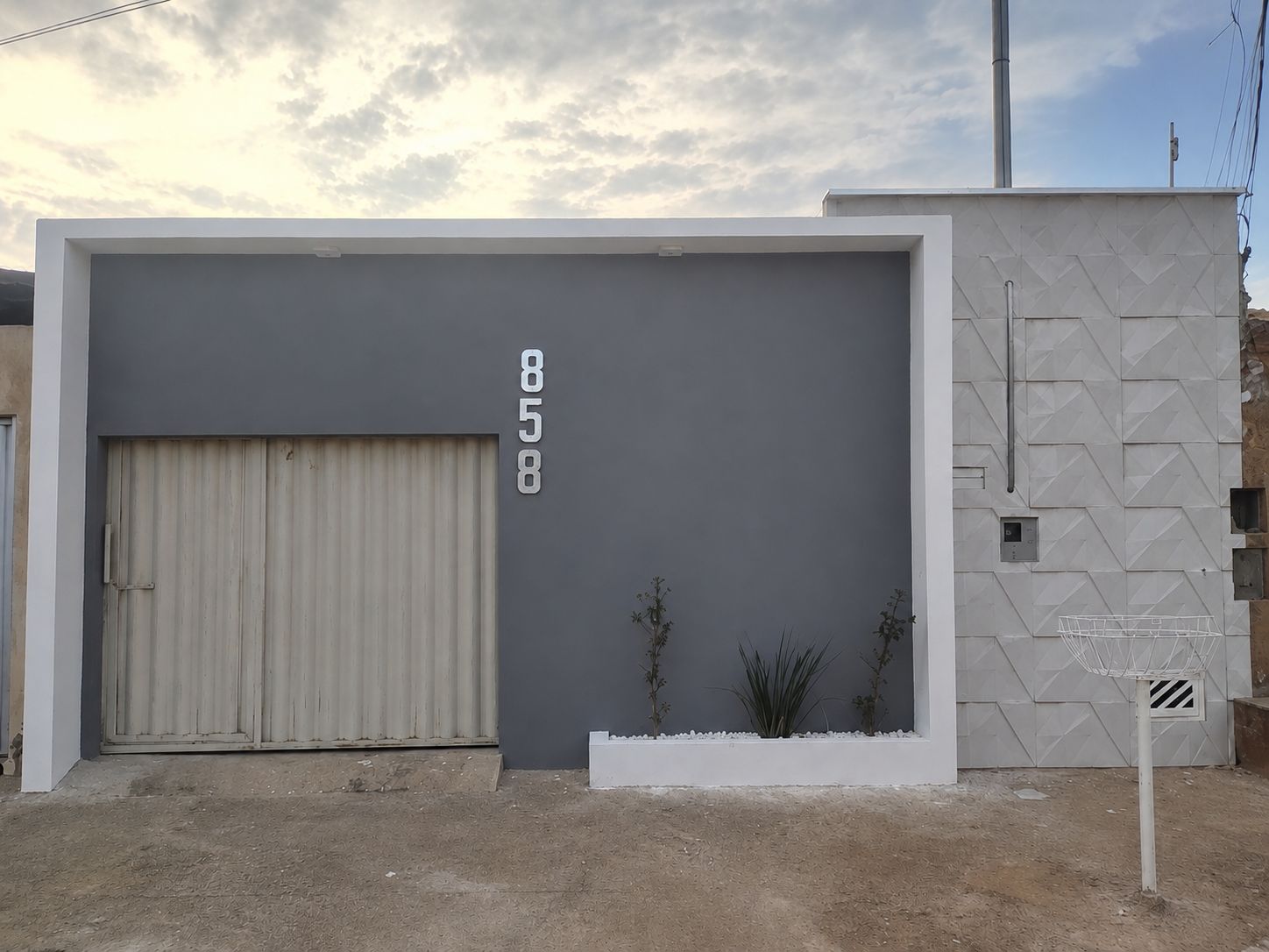 En moderne bygning med stor garageport, grå facade og en lille hvid plantekasse med planter.