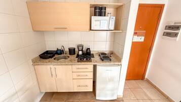 A compact kitchenette with a sink, coffee maker, kettle, and a small refrigerator.