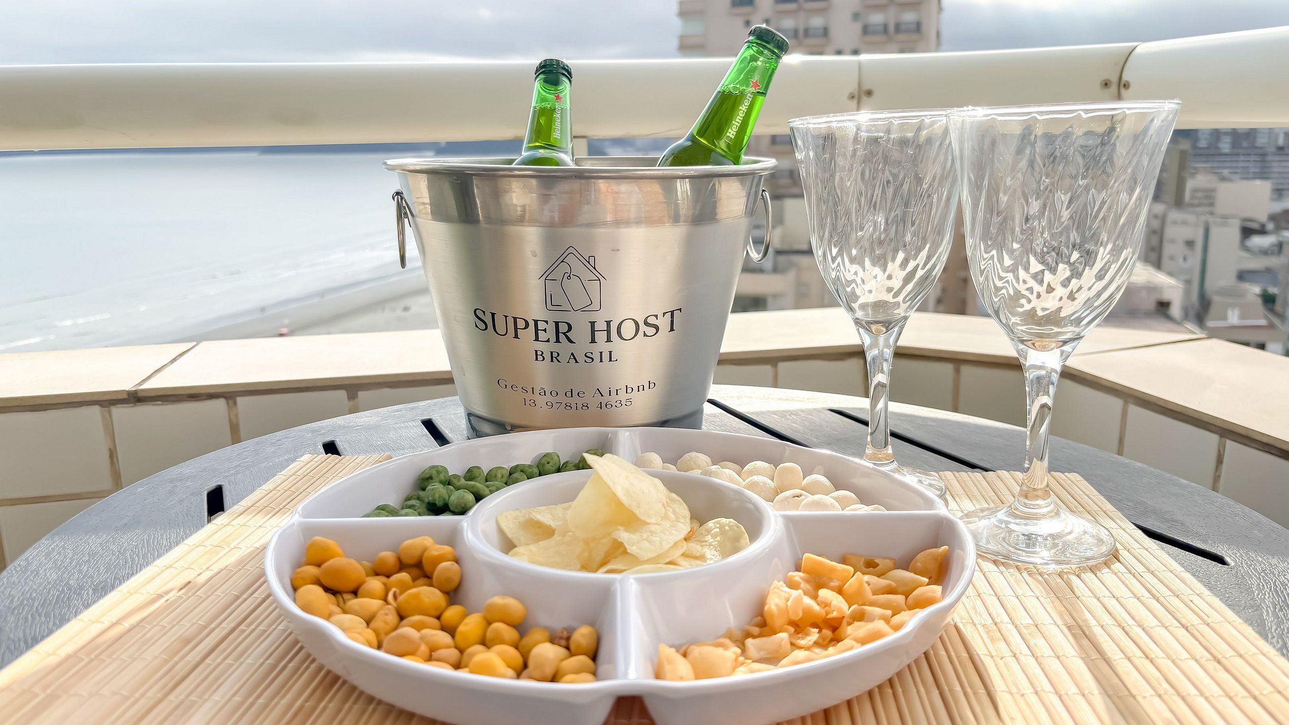 Una mesa con un balde de bebidas etiquetado 'SUPER HOST BRASIL', dos vasos y un plato con aperitivos.
