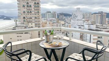A balcony with a table set for two, a view of the cityscape, and a beach in the background.