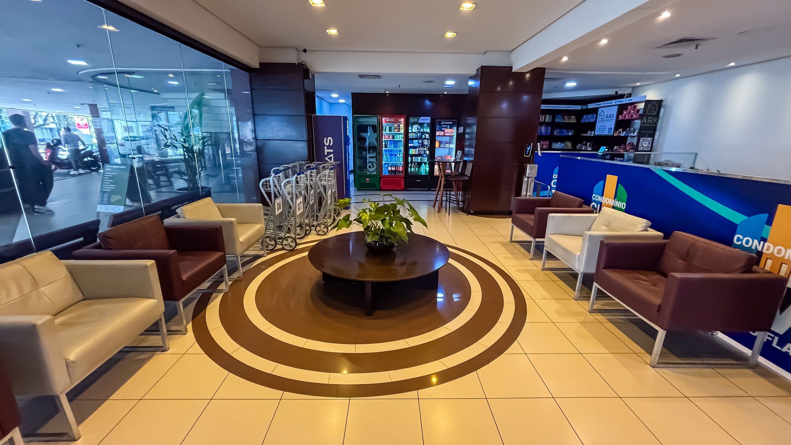 A modern lobby with a central circular seating area, a reception desk, and a view of the street outside.