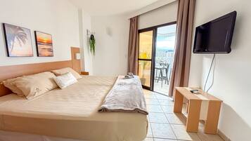 Habitación de hotel con cama, televisión, balcón con vistas y una pequeña mesa.
