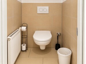 Ein kleines, modernes Badezimmer mit Toilette, Handtuchwärmer, Toilettenpapierhalter, Bidet und Mülleimer.