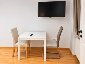 Ein modernes Zimmer mit einem weißen Tisch, zwei Stühlen, einem Fernseher an der Wand und einer Tür mit Vorhängen.