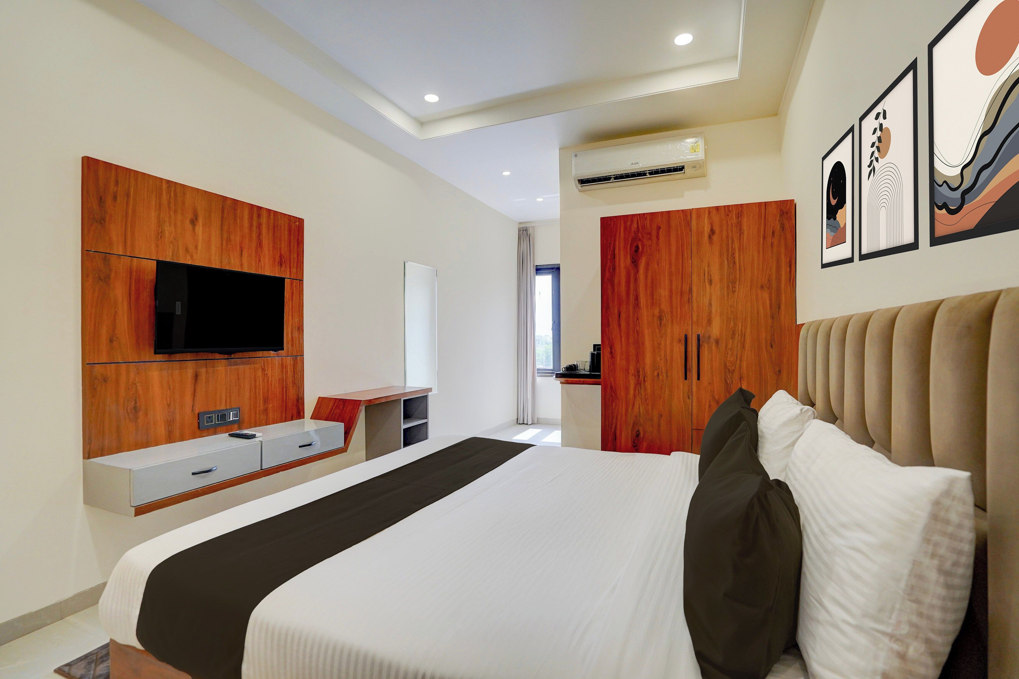 Habitación de hotel moderna con una cama grande, un televisor instalado en un panel de madera, un escritorio con una silla y una obra de arte en la pared.
