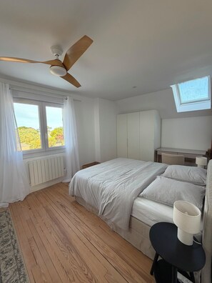 A bedroom with a bed, a ceiling fan, a window with curtains, a radiator, and a skylight. - L’Oasis – Family home for 12, enclosed garden, walk to beach (Saint-Pierre-Quiberon)