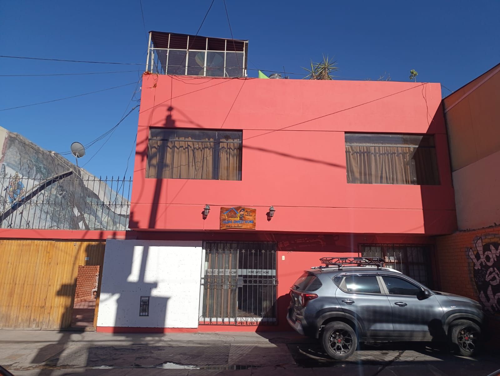 A two-story building with a red facade, a parked car, and a satellite dish.