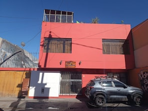 A two-story building with a red facade, a parked car, and a satellite dish. - homesweethome (Arequipa)
