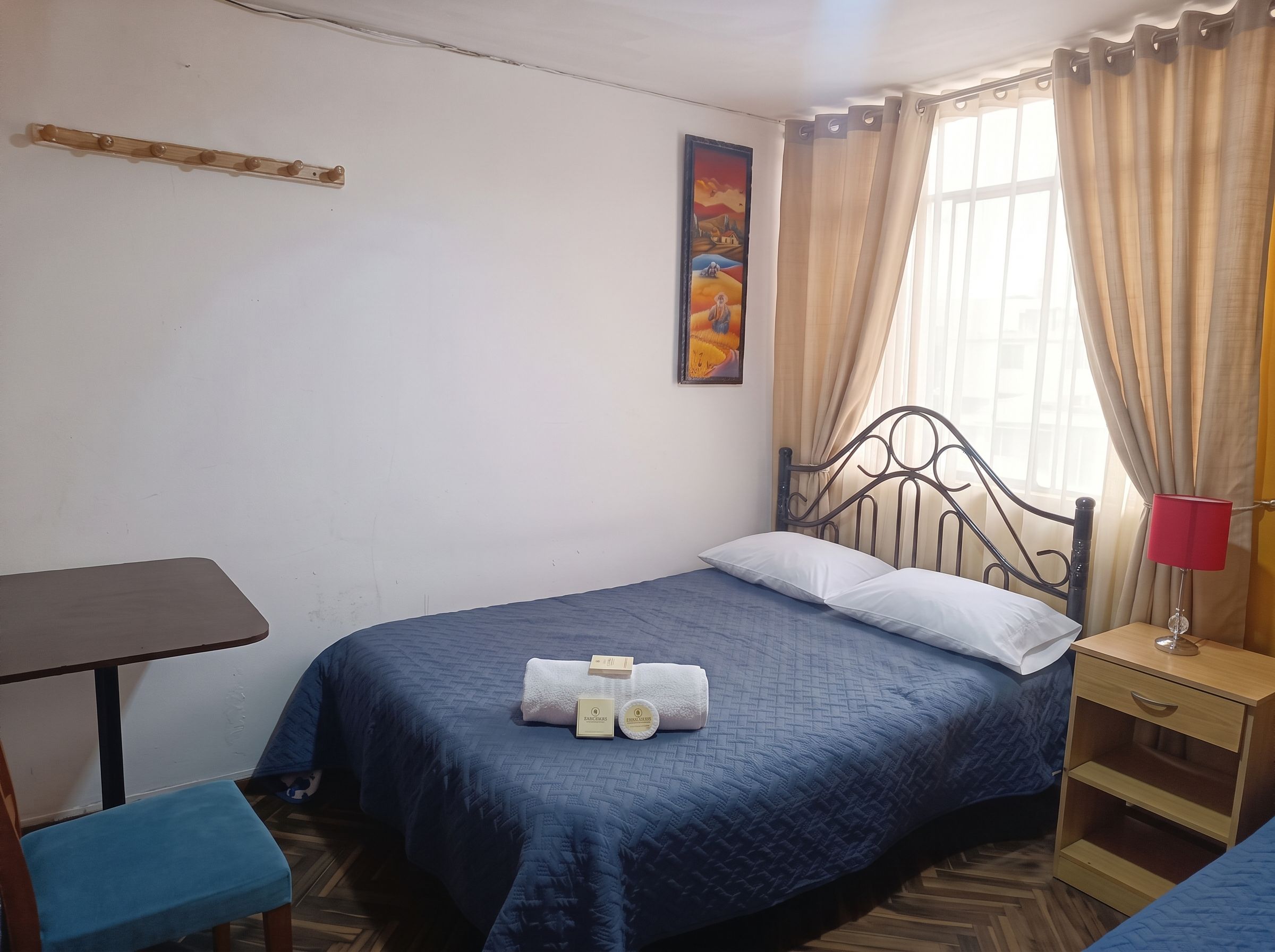 Un dormitorio con cama, mesita de noche, silla, ventana con cortinas y estante en la pared.