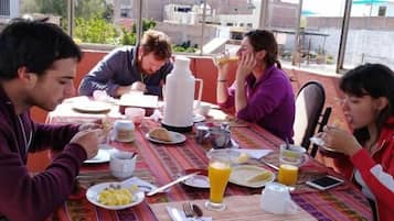Un grupo de personas cenando en una mesa al aire libre con vistas a edificios al fondo.