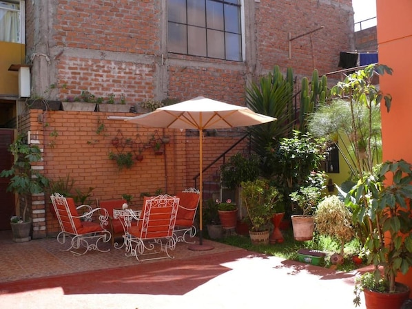 Un patio exterior con una mesa y sillas, rodeado de plantas en macetas y una pared de ladrillo.