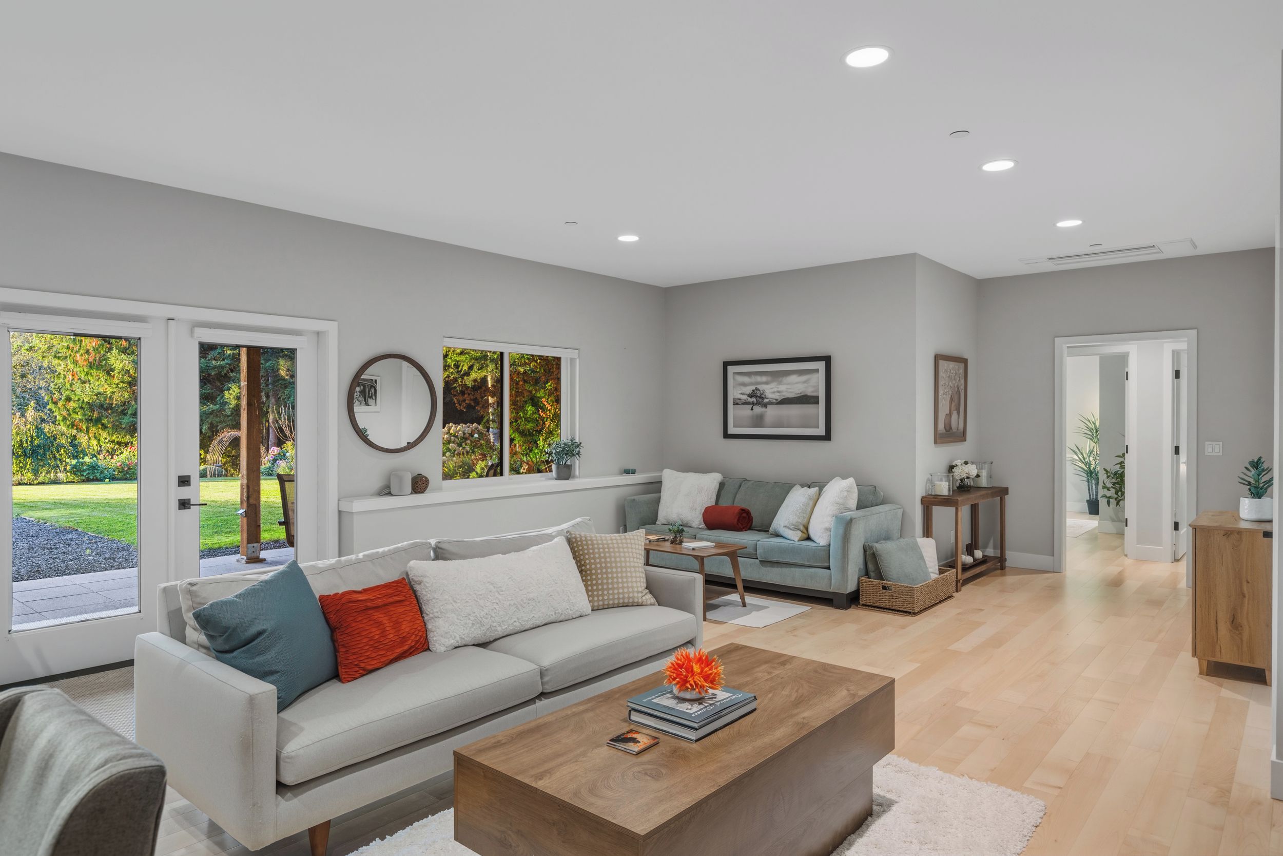 A modern living room with a sofa, coffee table, and a view of a garden through large windows.