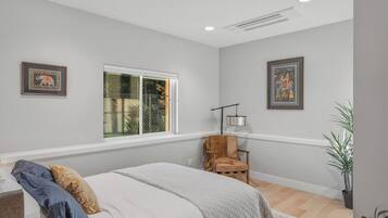 Une chambre à coucher avec un lit, une chaise, une fenêtre et deux tableaux encadrés accrochés au mur.
