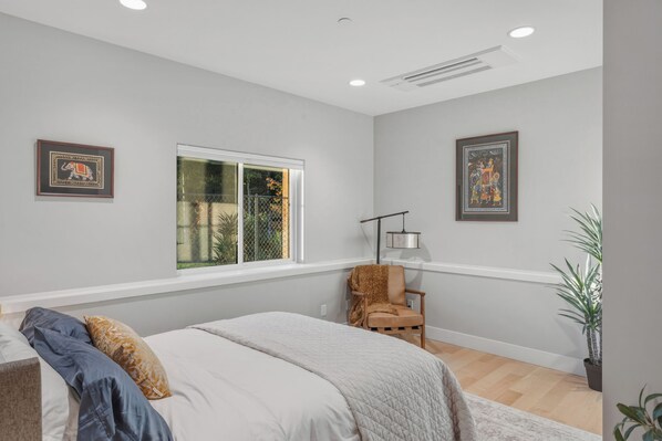A bedroom with a bed, a chair, a window, and two framed pictures on the wall.