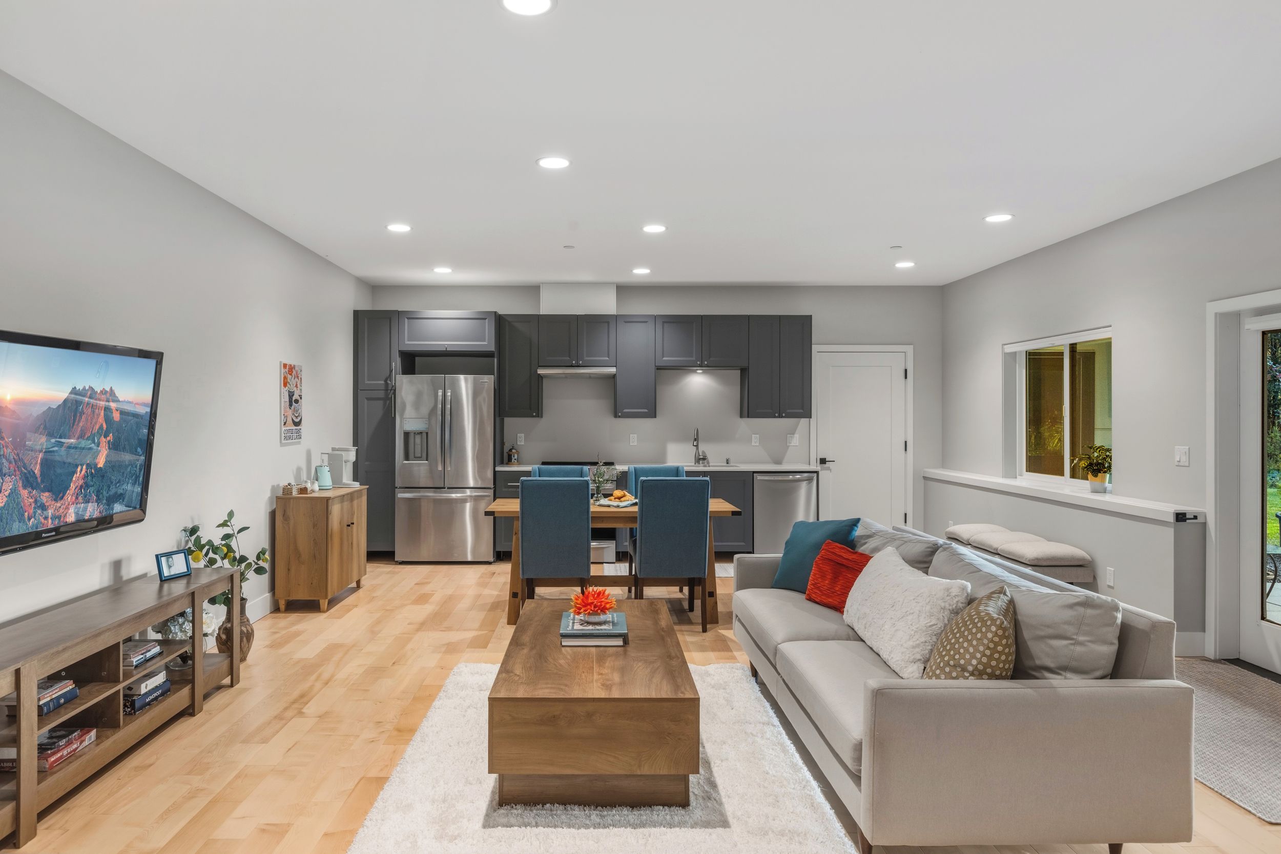 A modern apartment with a living room, dining area, kitchen, and a large window.
