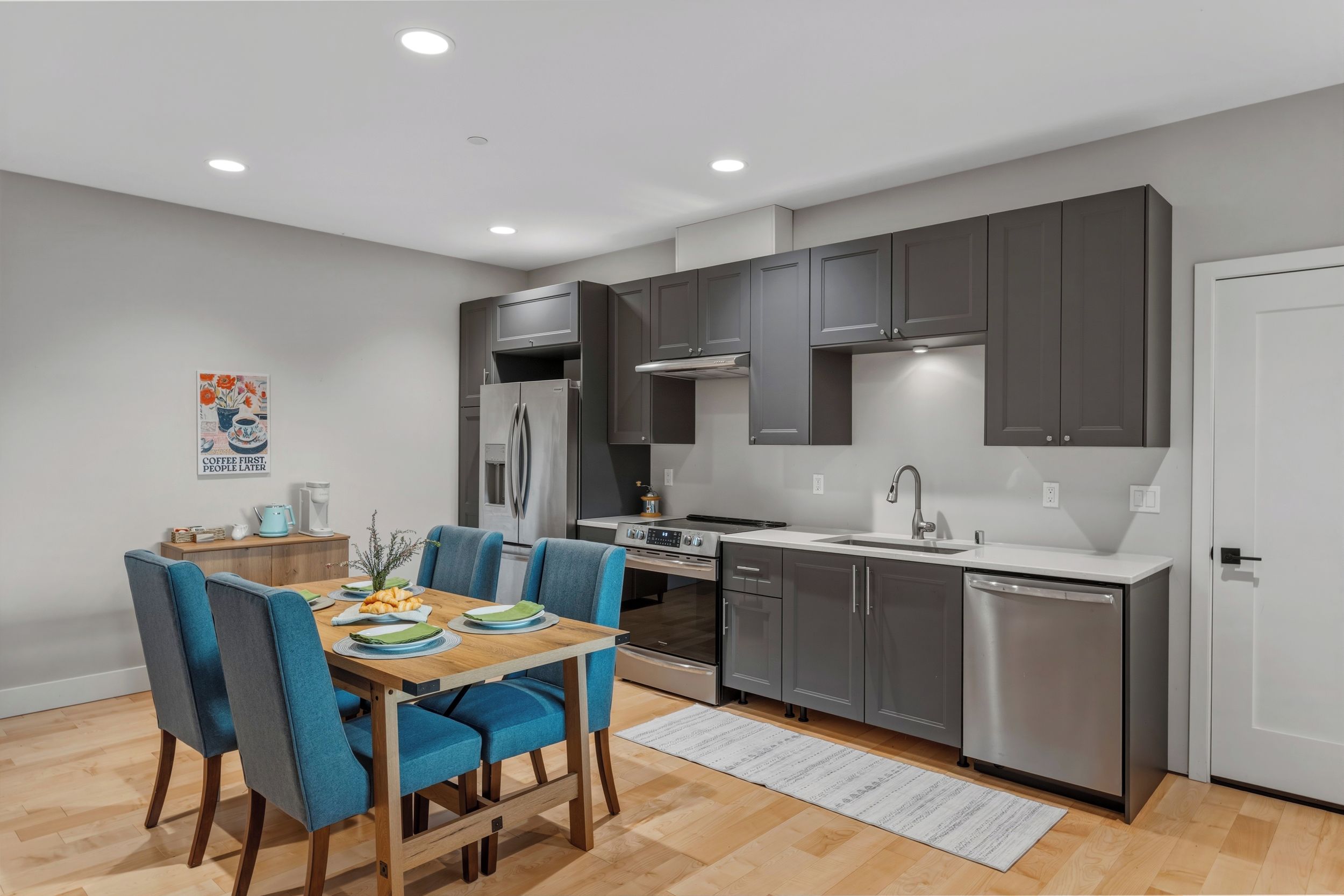 A modern kitchen with grey cabinets, stainless steel appliances, and a dining area with blue chairs.