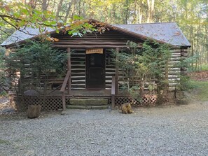 A rustic log cabin with a 'WELCOME' sign, surrounded by trees and a gravel path. - Black Bear Hideaway Cabin #6 (Clarington)