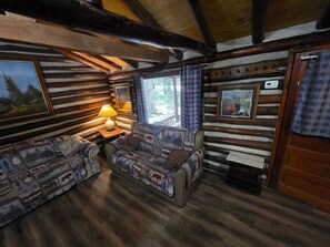 A log cabin interior with a sofa set, a lamp, and framed pictures on the walls. - Black Bear Hideaway Cabin #6 (Clarington)