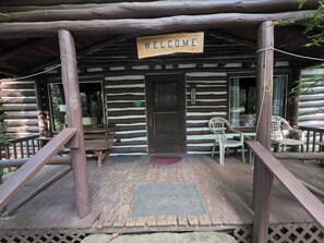 A wooden cabin with a 'WELCOME' sign, a porch with a ramp, and plastic chairs. - Black Bear Hideaway Cabin #6 (Clarington)