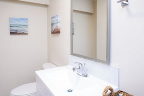 A bathroom with a white sink, chrome faucet, and a large mirror. There are two framed pictures on the wall.